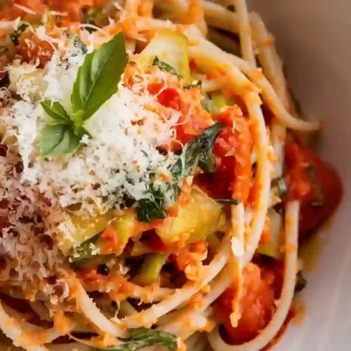 A bowl of brown rice pasta with sautéed cherry tomatoes, spinach, and fresh basil, served on a modern white plate.